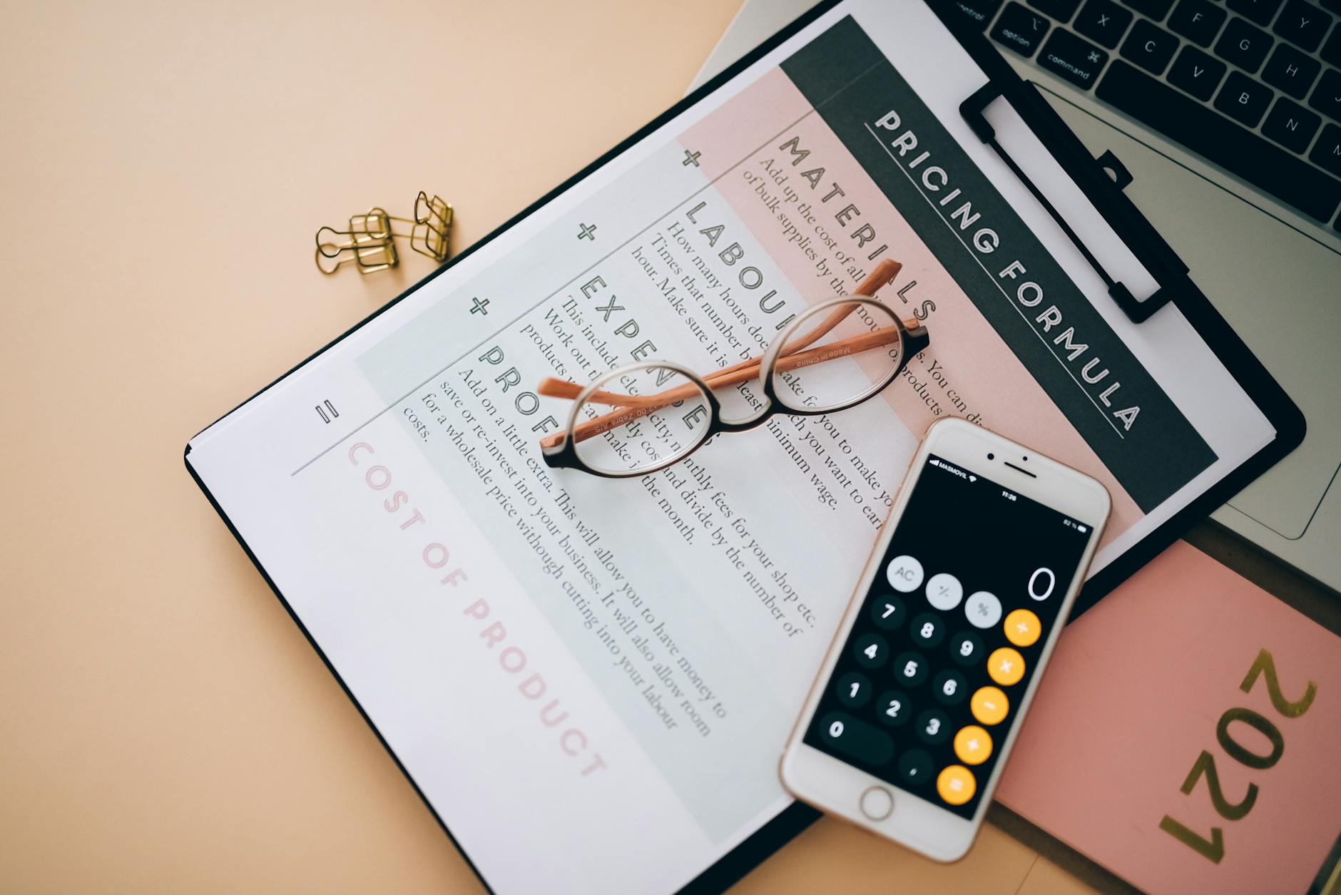 A pricing formula worksheet with glasses and a phone calculator on a desk