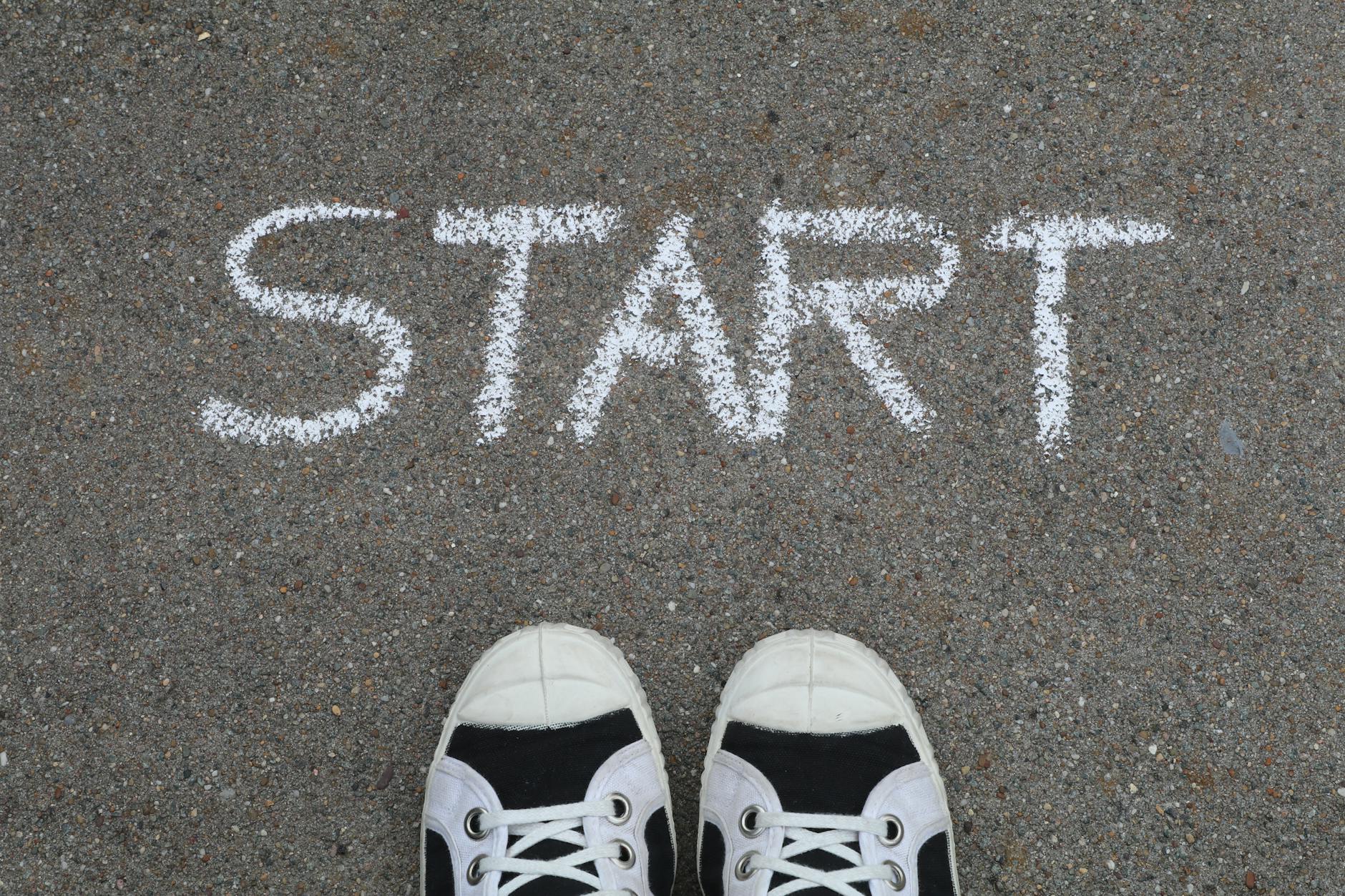 A pair of sneakers standing behind the word START written in chalk on pavement