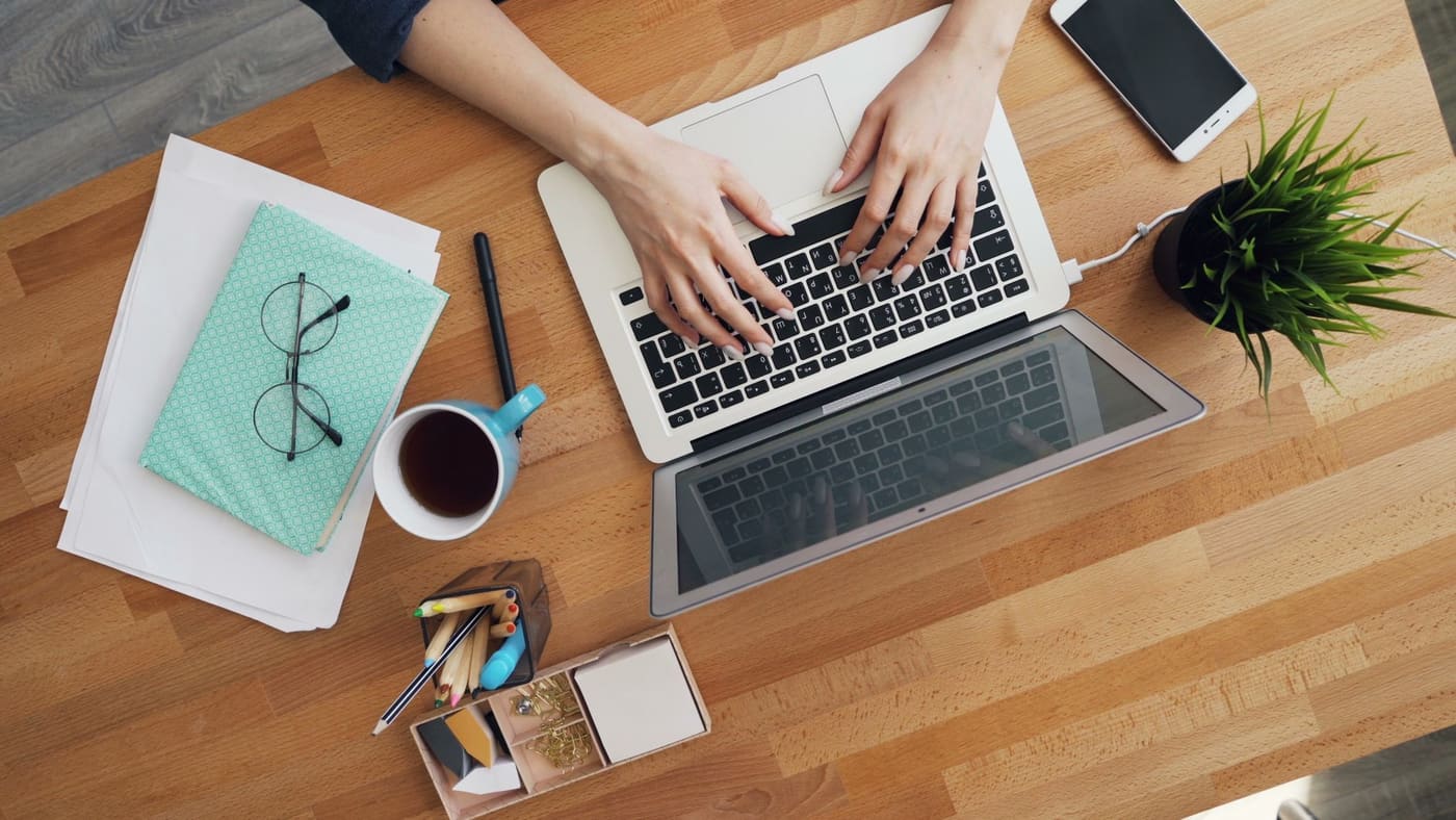 Overhead view of a laptop, notebook, phone and coffee on a wooden desk