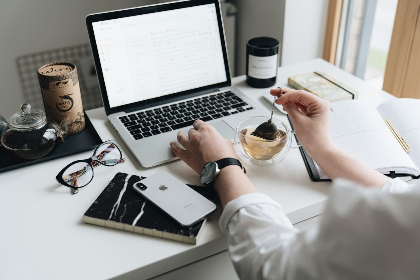 A laptop, cup of tea and notebook on a bright home-office desk