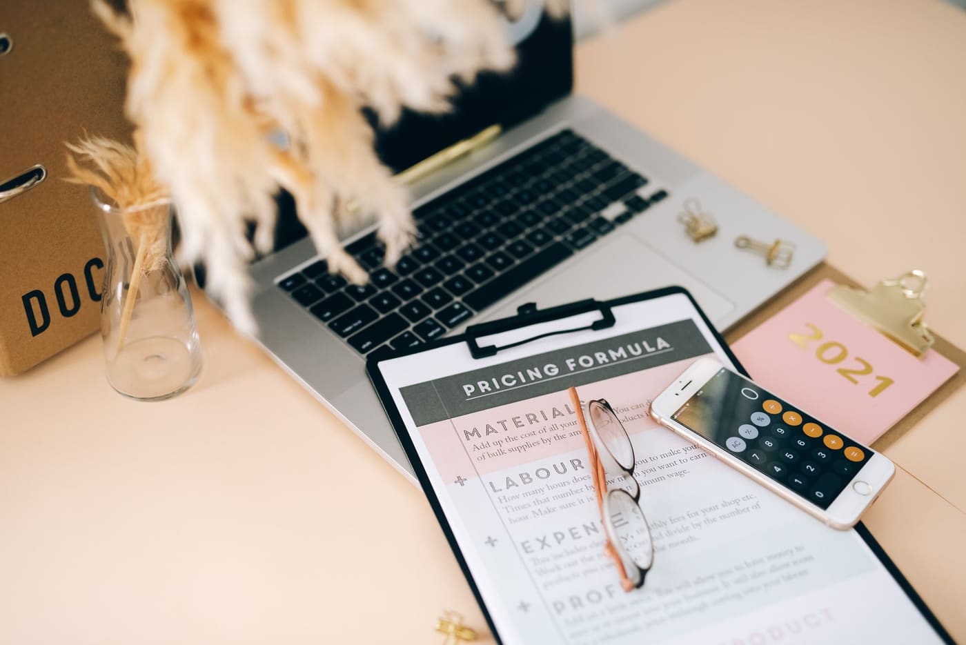 A clipboard with a pricing worksheet beside a phone calculator and laptop