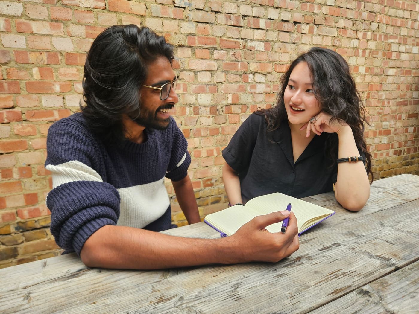 Two adults talking at a wooden table with a notebook open between them